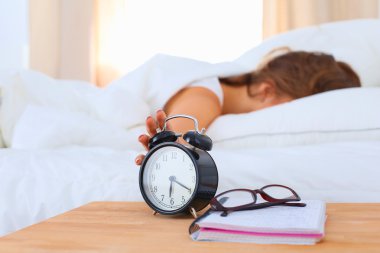 Young woman putting her alarm clock off in the morning clipart
