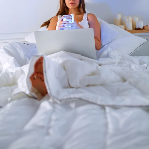 Młoda kobieta z laptopa w łóżku i cieszyć się filiżanką herbaty — Zdjęcie stockowe