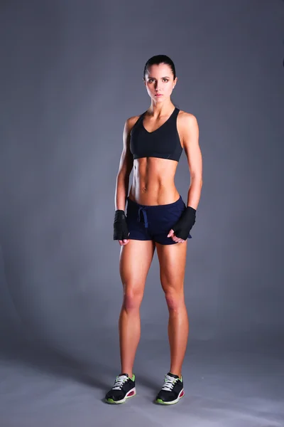 Muscolare giovane donna in posa in abbigliamento sportivo contro sfondo nero — Foto Stock