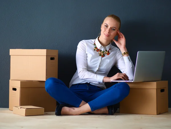 Woman sitting on the floor near a boxes with laptop — Stock Photo, Image