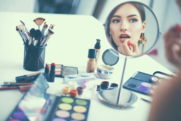 Joven hermosa mujer haciendo maquillaje cerca del espejo, sentado en el escritorio —  Fotos de Stock