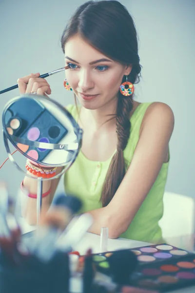 Jeune belle femme se maquillant près du miroir, assise au bureau — Photo