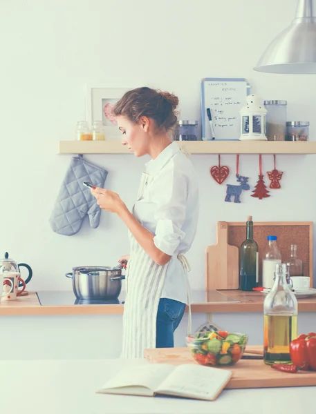 Retrato de una mujer sonriente con teléfono en la cocina en casa — Foto de Stock