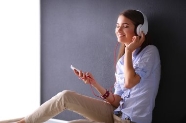 Duvara yakın katta oturan kulaklıklar ile gülümseyen kız