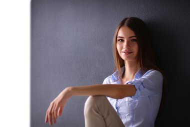 Genç bir kadın yerde, kara duvarın yanında oturuyor.