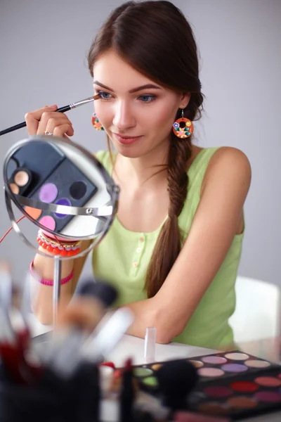 Junge schöne Frau schminkt sich in der Nähe des Spiegels und sitzt am Schreibtisch — Stockfoto