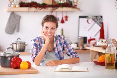 Mutfakta yemek kitabı okuyan genç bir kadın yemek tarifi arıyor.