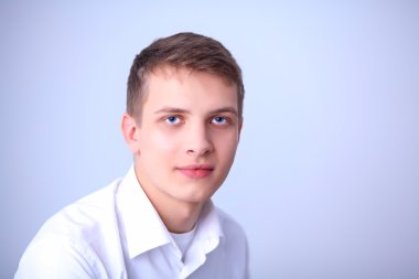 Gri arka plan üzerinde oturan gülümseyen genç adam portresi