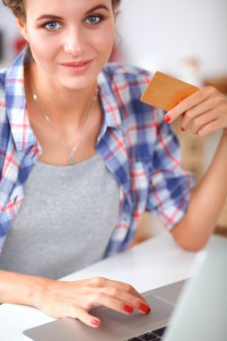 Mutfakta bilgisayar ve kredi kartı kullanan gülümseyen bir kadın.