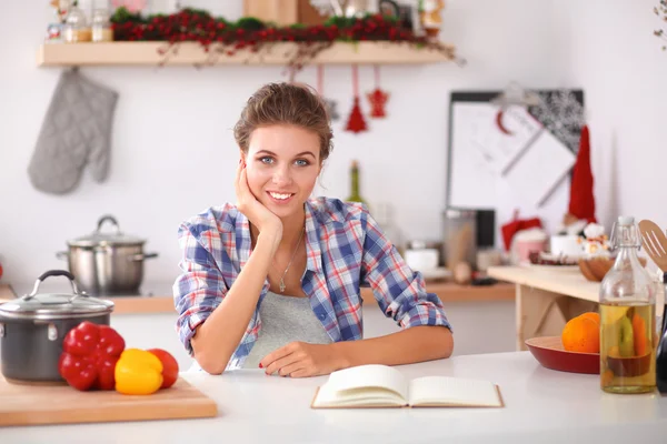 Jovem mulher lendo livro de receitas na cozinha, à procura de receita — Fotografia de Stock