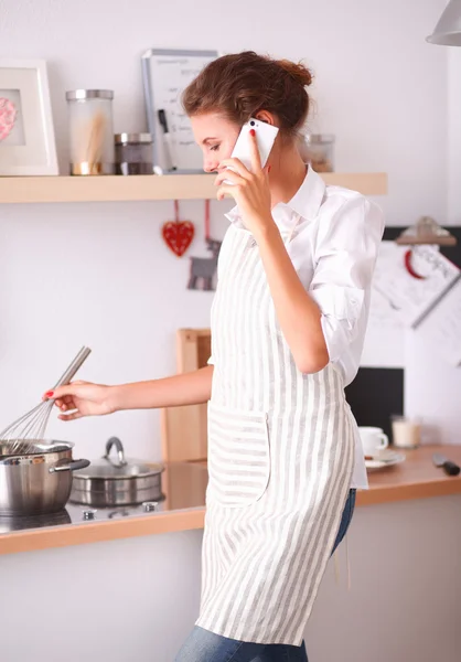 Retrato de una mujer sonriente con teléfono en la cocina en casa — Foto de Stock