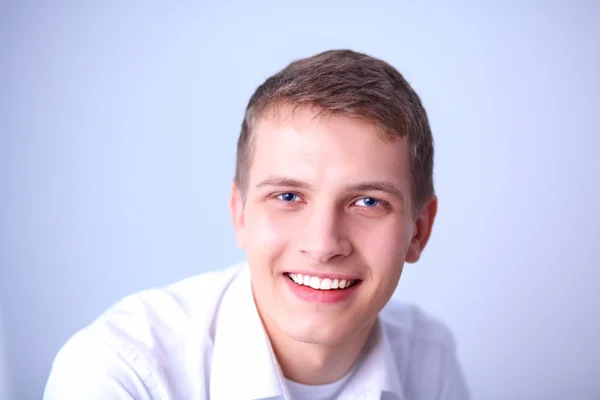 Portrét mladého muže s úsměvem, sedí na šedém pozadí — Stock fotografie
