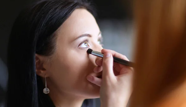 Joven hermosa mujer haciendo maquillaje cerca del espejo, sentado en el escritorio . — Foto de Stock