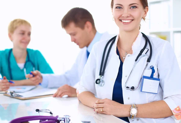 Bonito jovem sorridente médico feminino sentado na mesa — Fotografia de Stock