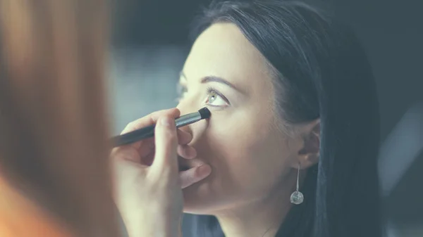 Joven hermosa mujer haciendo maquillaje cerca del espejo, sentado en el escritorio . — Foto de Stock