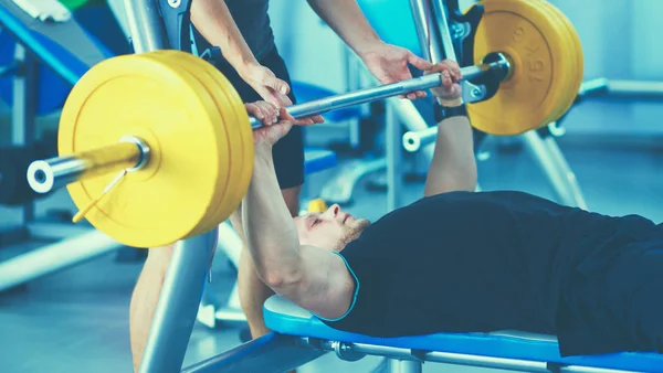 Jeune homme levant la barre dans la salle de gym avec instructeur — Photo