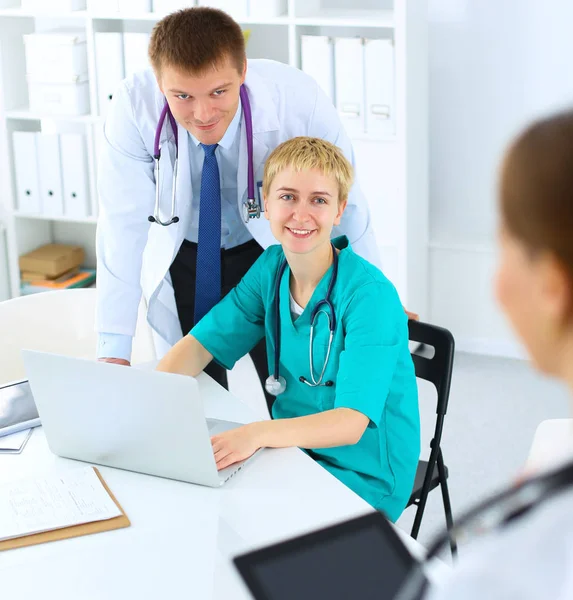 Schöne junge lächelnde Ärztin sitzt am Schreibtisch — Stockfoto
