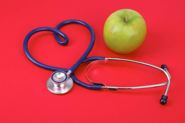 Green apple and stethoscope isolated on red background