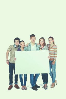 Beyaz arka planda izole edilmiş boş bir tahta tutan bir grup genç arkadaş.