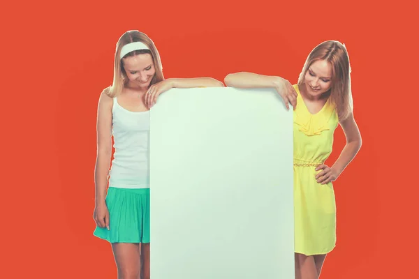 Retrato de dos mujeres jóvenes casuales de pie cerca de la tarjeta en blanco sobre fondo blanco — Foto de Stock