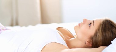 Güzel genç bir kadın, rahat ve mutlu bir şekilde yatakta uzanıyor.