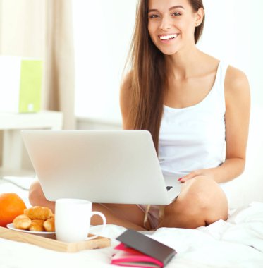 Dizüstü bilgisayar ile yatakta oturan genç güzel kadın