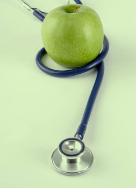 Stetoskop ve yeşil elma beyaz arkaplanda izole edilmiş.