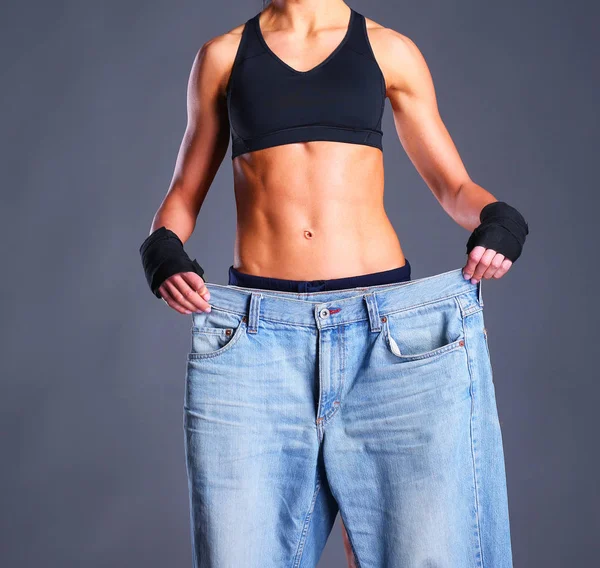 Молодая фитнес-женщина показывает, что ее старые джинсы — стоковое фото