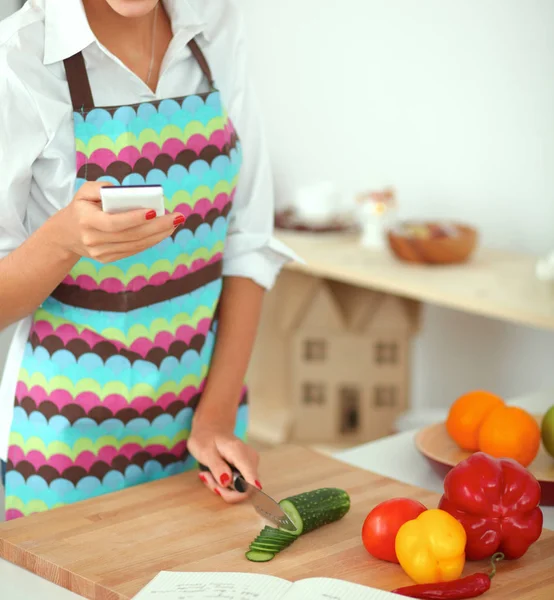 Mujer sonriente sosteniendo su teléfono celular en la cocina — Foto de Stock