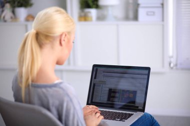 Genç ve güzel bir kadın evde dizüstü bilgisayar kullanıyor.