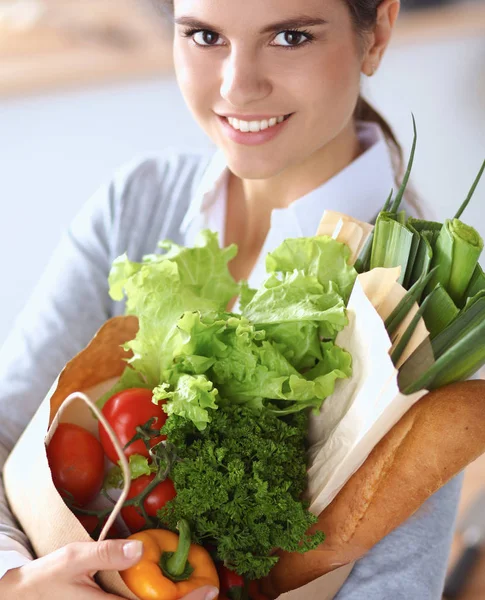 Młoda kobieta trzyma torbę na zakupy z warzywami Stojąc w kuchni — Zdjęcie stockowe