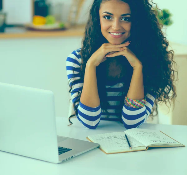 Sorrindo jovem com xícara de café e laptop na cozinha em casa — Fotografia de Stock