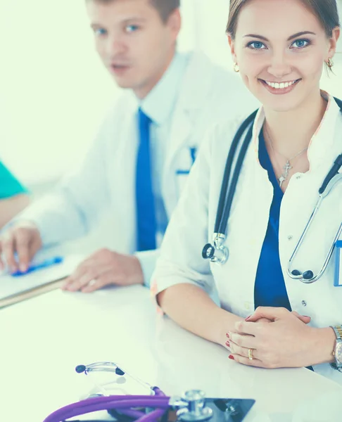 Bonito jovem sorridente médico feminino sentado na mesa — Fotografia de Stock