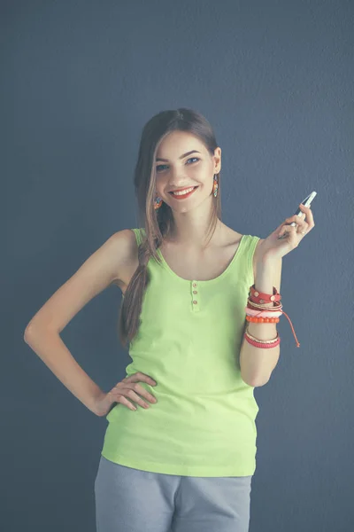 Young woman standing near dark wall with mobile phone — Stock Photo, Image