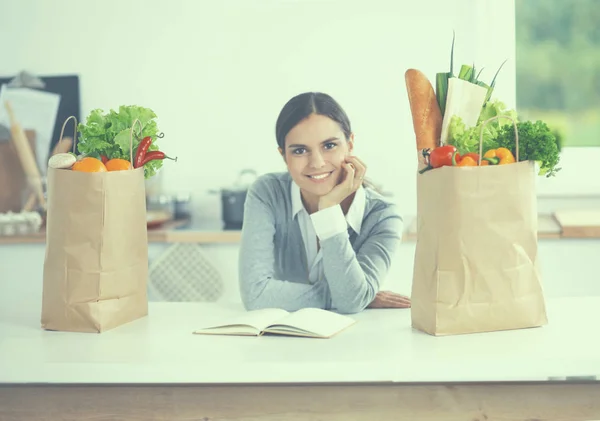 Een jonge vrouw die een boodschappentas met groenten vasthoudt. Staande in de keuken — Stockfoto