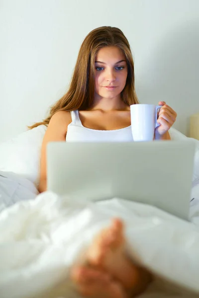 Młoda kobieta z laptopa w łóżku i cieszyć się filiżanką herbaty — Zdjęcie stockowe