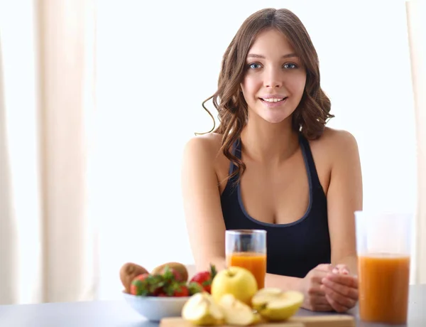 Flicka sitter i köket på skrivbordet med frukt och glas juice — Stockfoto