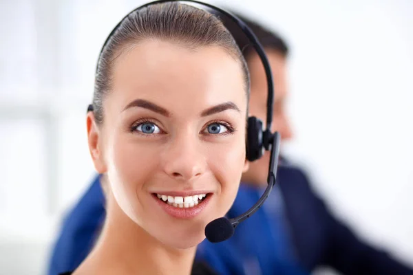 Retrato de mujer de negocios hermosa en auriculares sonriendo con colegas de fondo — Foto de Stock