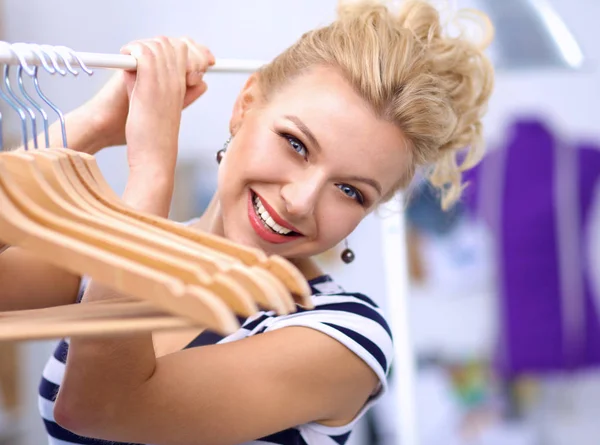 Mooie jonge stylist in de buurt van rack met hangers in office — Stockfoto