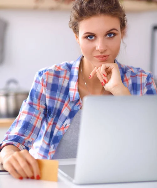 Mujer sonriente compras en línea utilizando la computadora y la tarjeta de crédito en la cocina — Foto de Stock