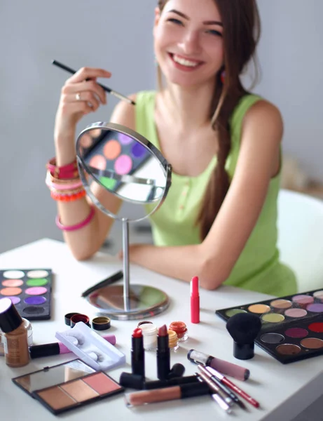 Joven hermosa mujer haciendo maquillaje cerca del espejo, sentado en el escritorio — Foto de Stock