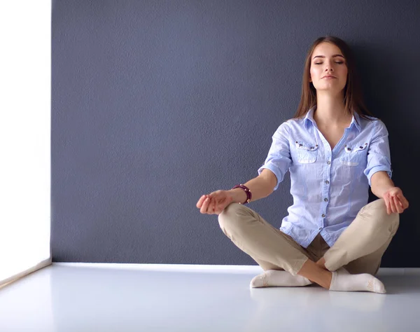 Genç bir kadın yerde, kara duvarın yanında oturuyor.