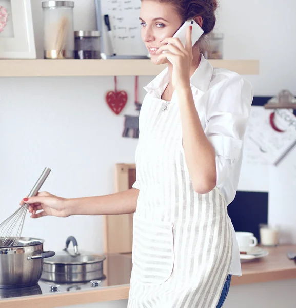 Портрет улыбающейся женщины с телефоном на кухне дома — стоковое фото