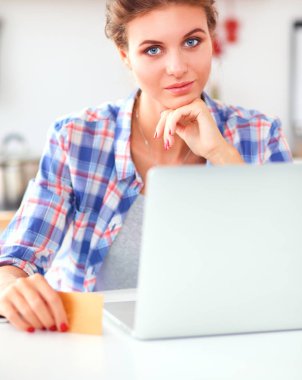 Mutfakta bilgisayar ve kredi kartı kullanan gülümseyen bir kadın.