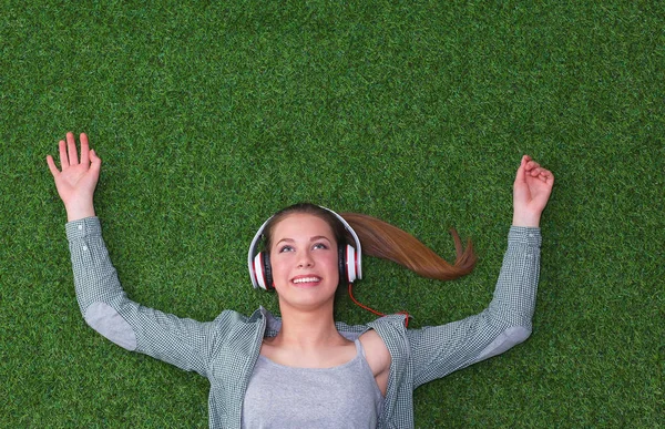 Relaxed woman listening to the music with headphones lying on  grass — Stock Photo, Image