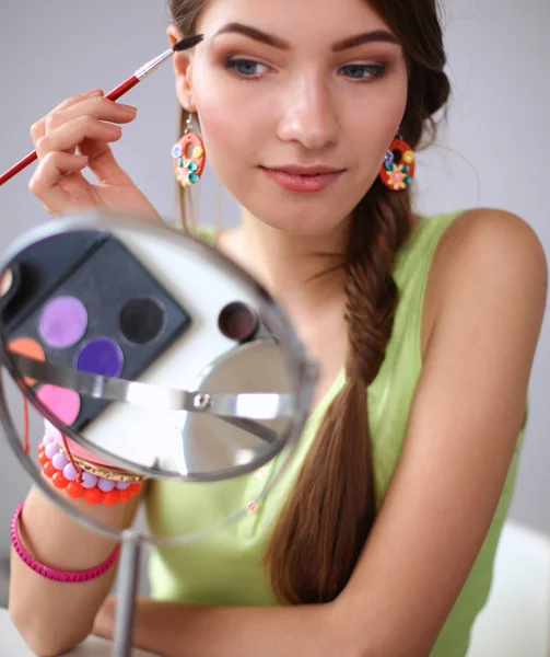 Молодая красивая женщина делает макияж возле зеркала, сидит за столом — стоковое фото