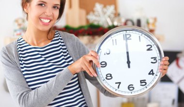 Mutlu genç kadın Noel süslemeli mutfakta saat gösteriyor.