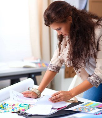 Gülümseyen kadın moda tasarımcısı ofis masasında oturuyor.