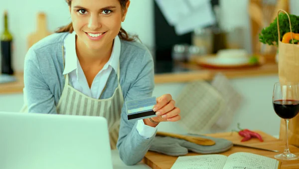 Lachende vrouw online winkelen met behulp van computer en creditcard in de keuken — Stockfoto