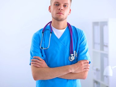 Steteskoplu doktor ayakta, çapraz kollu, beyaz arka planda izole.